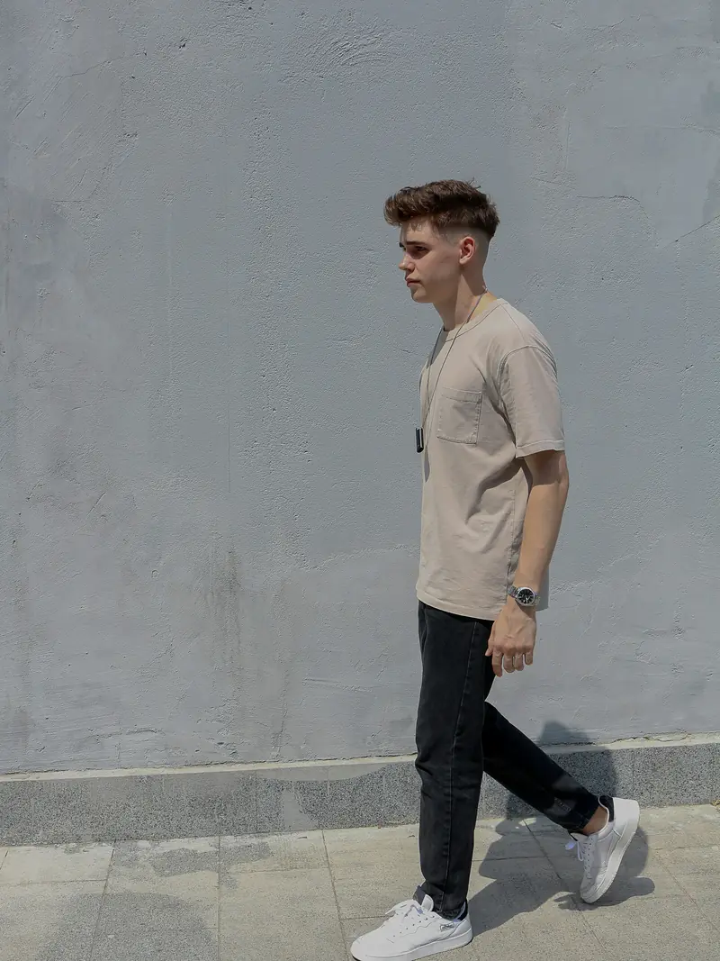 Stone tee and black trousers, walking past a grey wall