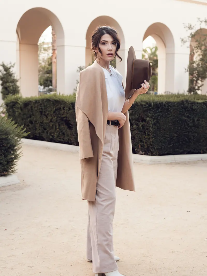 Camel coat and wide-brim hat beneath stone arches